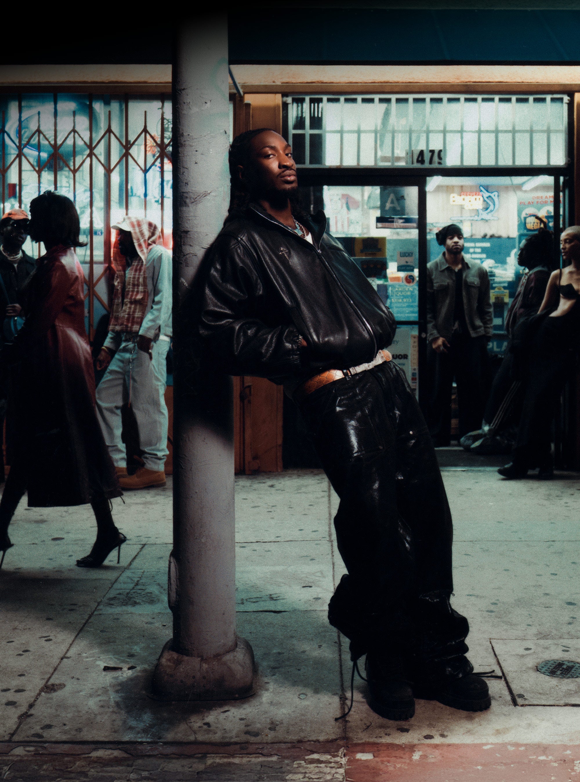 Man in a black leather outfit standing on a city street with people in the background.