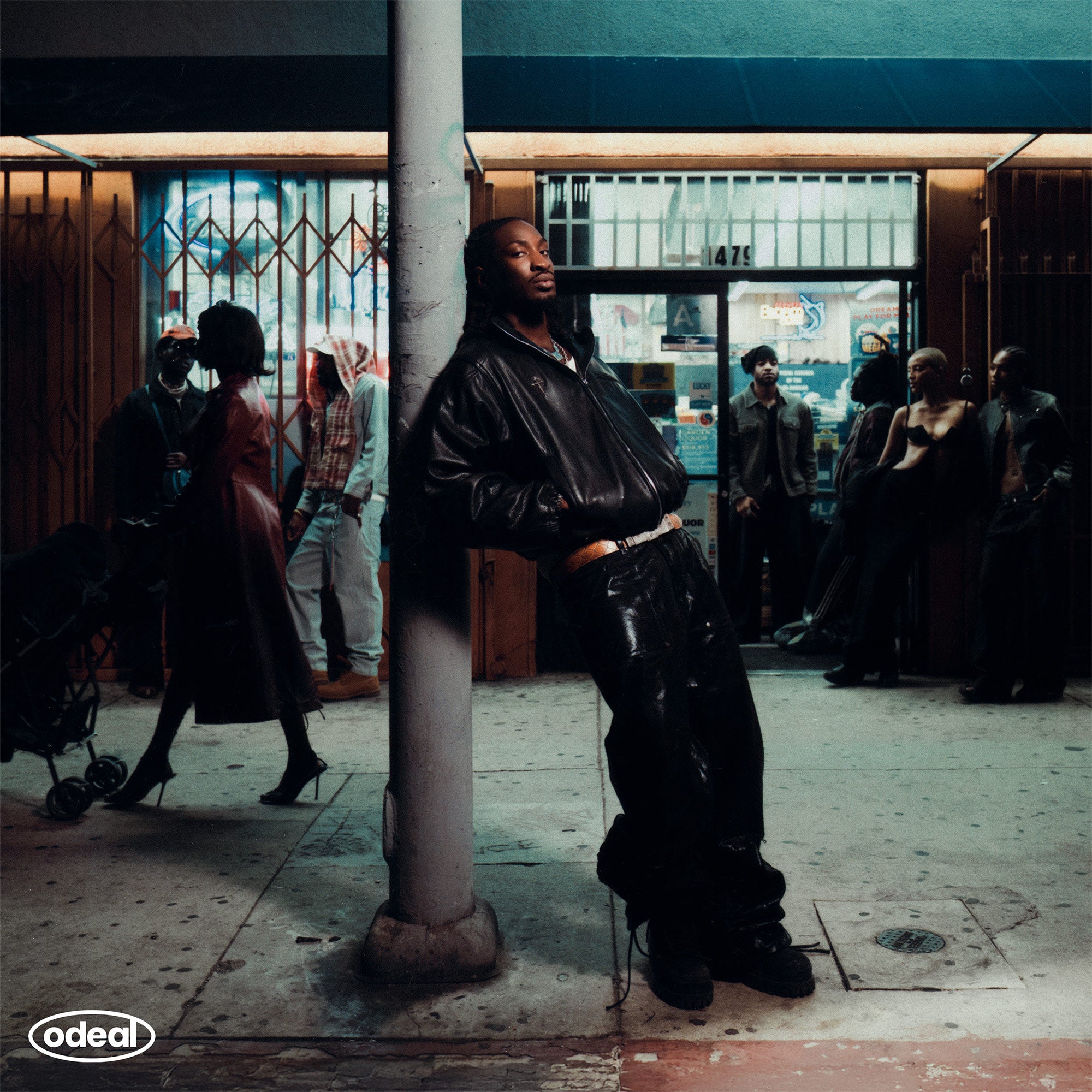 Person in black leather outfit leaning against a pole in an urban setting with 'odeal' branding.
